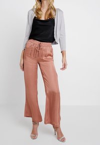 Ljusgrå kort cardigan, svart satin tank top och persikofärgade vida byxor. Byxorna har elastisk midja och en slät textur.