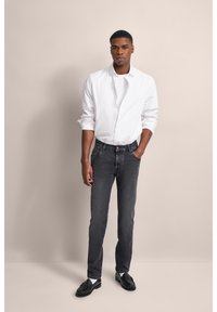 Jeans in denim grigio abbinati a una camicia bianca con bottoni. Le scarpe sono nere, con una texture liscia e un design classico. Sfondo semplice.