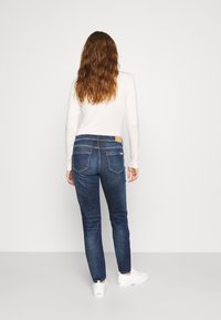 Smala jeans i mörkblå denim, med en midja i normalhöjd, bakfickor och en läderlapp på midjebandet. Matchat med vita sneakers.