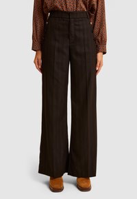 Szerokie spodnie z wysokim stanem w ciemnobrązowym kolorze z cienkimi pionowymi paskami. Posiadają boczne guziki i dopasowany krój. Połączone z beżowymi botkami za kostkę.