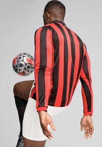 Rood en zwart gestreepte sportshirt met lange mouwen, gecombineerd met witte shorts, met een voetbalt aan het bewegen. Kenmerken zijn logo-details.