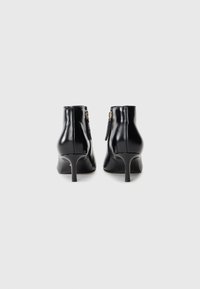 Bottines noires en cuir avec un bout pointu, un talon fin et une fermeture éclair sur le côté. Texture lisse avec des accents en métal doré sur les zips.