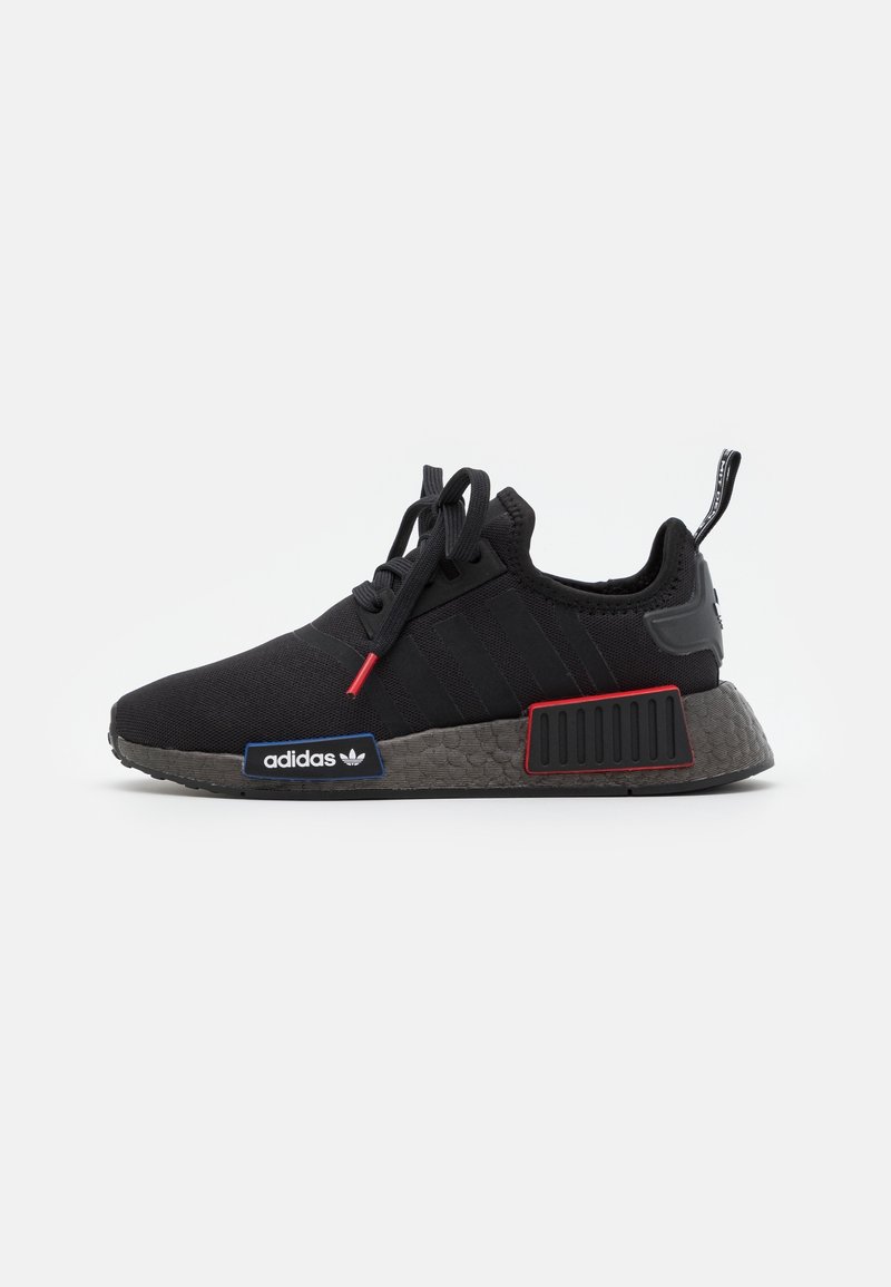 Black adidas NMD sneakers featuring a textured upper, three stripes, red accents, and a patterned gray sole with branding.