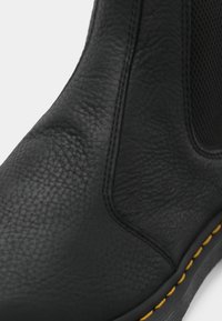 Botte en cuir noir à surface texturée, avec un accent de couture jaune le long de la semelle et un panneau en mesh sur le côté pour la respirabilité.