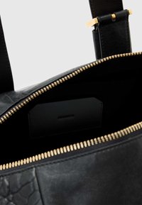 Zwarte leren tas met gouden ritssluiting, voorzien van een zwart vak voor kaarten en een gestructureerd paneel. Glad afgewerkt met een strak ontwerp.