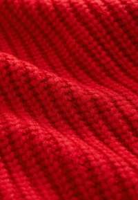 Tessuto rosso lavorato a maglia con motivi testurizzati e in rilievo. Il materiale appare morbido e peloso, mostrando una tonalità profonda e vivace in tutto il suo insieme.