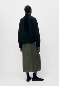 Giacca bomber nera con vestibilità rilassata, abbinata a una lunga gonna verde oliva. Capelli intrecciati e calzature nere completano il look.