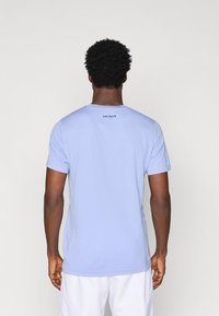 Ανοιχτό μπλε κοντομάνικο T-shirt με στρογγυλή λαιμόκοψη, έχοντας ένα διακριτικό λογότυπο Lacoste στο πίσω μέρος. Κατασκευασμένο από μαλακό και απαλό ύφασμα.