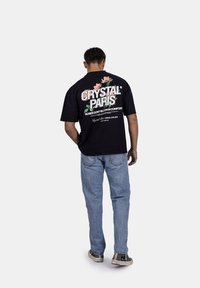 Černé bavlněné tričko s grafickým potiskem na zádech, zdobené květinovými akcenty, textem "CRYSTAL PARIS" a "RŮŽE NEKVNÉ V POHODLÍ".