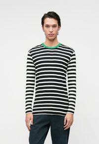 Langermet stripete skjorte i svart og hvitt med grønn krage. Har horisontale striper og er laget av et mykt, teksturert stoff.