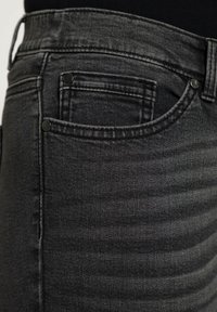 Musta farkkuhousut ovat slim fit -malliset, tekstuuripinnalla ja niissä on kaksi takataskua mustilla yksityiskohdilla. Ompeleet ovat huomaamattomat ja tasaiset.