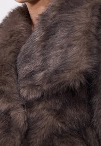 Manteau en fausse fourrure marron avec un large col, présentant une surface douce et texturée ainsi que de subtiles variations d'ombrage et de longueur de la fourrure.