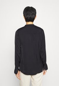 Sort langærmet skjorte lavet af glat stof, med en plisseret tekstur på ærmerne og rygpanelet, samt en afslappet pasform.