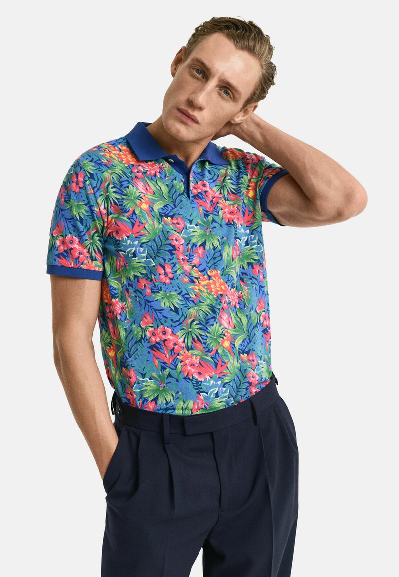 Herren-Polohemd mit kurzen Ärmeln in Blau, versehen mit einem lebhaften floralen Design in Rot, Pink und Grün; verfügt über einen klassischen Kragen und eine taillierte Silhouette.
