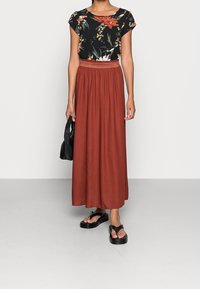 Top nero floreale con maniche a cappuccio, abbinato a una gonna maxi fluida color ruggine. Infradito nere e una borsa nera completano il look.