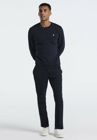 Marineblauwe sweatshirt met geribbelde manchetten en een ronde halslijn, gecombineerd met bijpassende marineblauwe broek. Model draagt witte sneakers. Eenvoudig ontwerp.