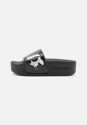 Sandale à glissière noire avec semelle épaisse, ornée d'un visage de dessin animé portant des lunettes de soleil et une cravate sur la bride, avec la marque "Karl Lagerfeld" sur le côté.