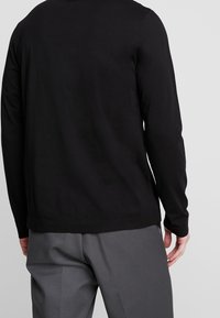 Black long-sleeve shirt made of cotton, featuring a crew neck, straight hem, and a smooth texture, worn with gray trousers.