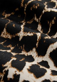 Tissu noir avec un motif léopard beige et marron irrégulier, montrant la texture et des plis.