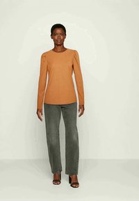 Blusa laranja de manga longa canelada com decote redondo e mangas ligeiramente bufantes, combinada com jeans cinza de cintura alta e sandálias de salto pretas.