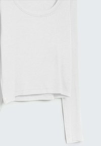 Valkoinen pitkähihainen paita, jossa on pyöreä pääntie, ribbikuviointi ja suora helma. Sisältää sivusaumat ja yksinkertaisen, minimalistisen muotoilun.