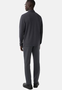 Grå langærmet polo med opslået krave, kombineret med grå bukser. Glat stof og afslappet pasform med diskrete syninger og blød tekstur.