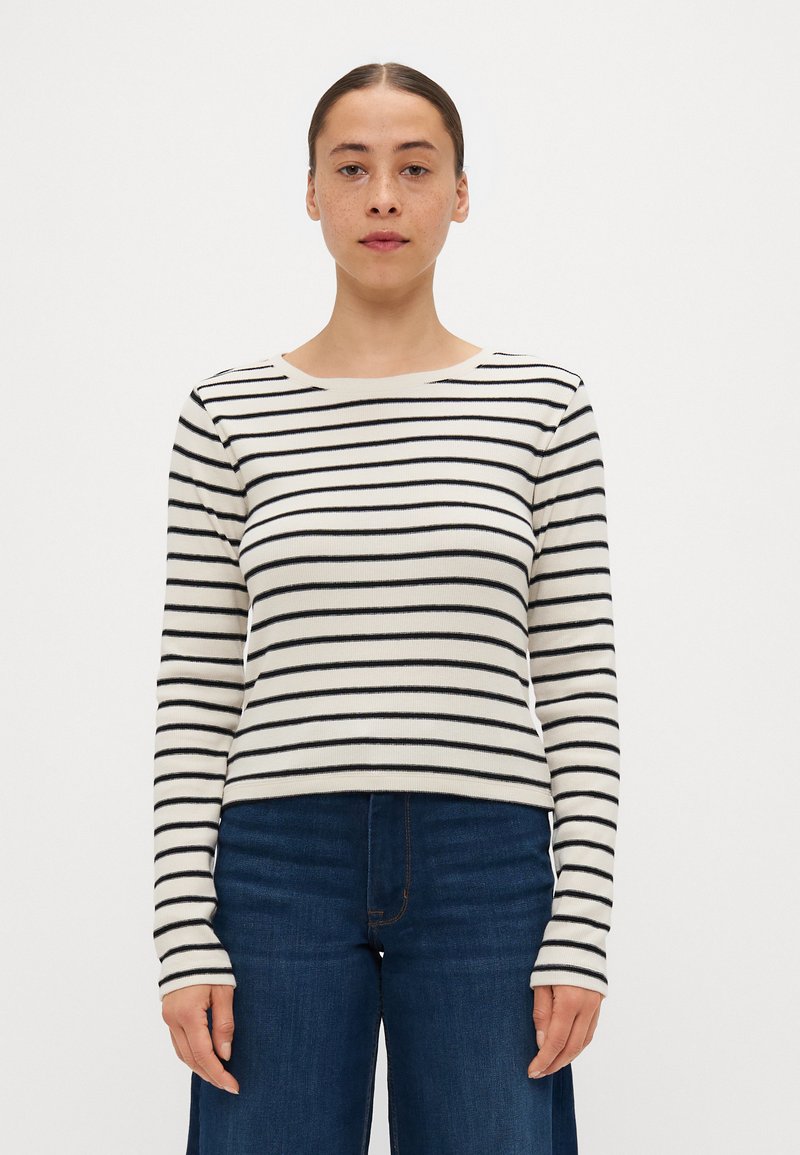 Stripet langermet topp i beige med svarte striper, rund hals, ribbet tekstur, kombinert med blå høy midje jeans.