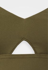 Top verde oliva com textura canelada e decote em V. Apresenta um detalhe recortado em forma triangular nas costas, realçando o design.