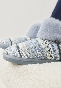 Chaussons tricotés dans une palette de couleurs bleue et grise, avec une tige à motifs, un bord doux en fausse fourrure grise et une semelle texturée grise.