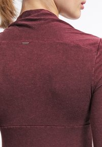 Mörkröd långärmad topp med en jämn yta, med en subtil sömnadsdesign och en liten logotags placerad nära halslinningen.