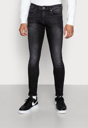 Jeans negros ajustados con un acabado ligeramente desgastado, que presentan cinco bolsillos y un cierre de botón en la parte delantera. Combinados con zapatillas negras.