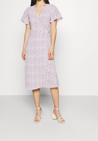Lilac-värinen kukkakuosiset mekko, jossa on lyhyet liehuvat hihat, V-pääntie ja midi-pituus. Yhdistetty vaaleanbeigeihin paksupohjaisiin sandaaleihin.