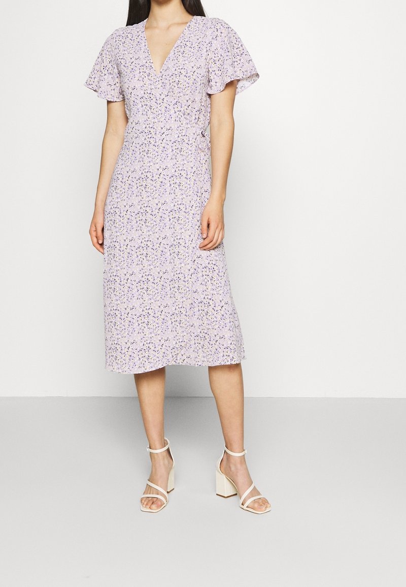Lilac-värinen kukkakuosiset mekko, jossa on lyhyet liehuvat hihat, V-pääntie ja midi-pituus. Yhdistetty vaaleanbeigeihin paksupohjaisiin sandaaleihin.