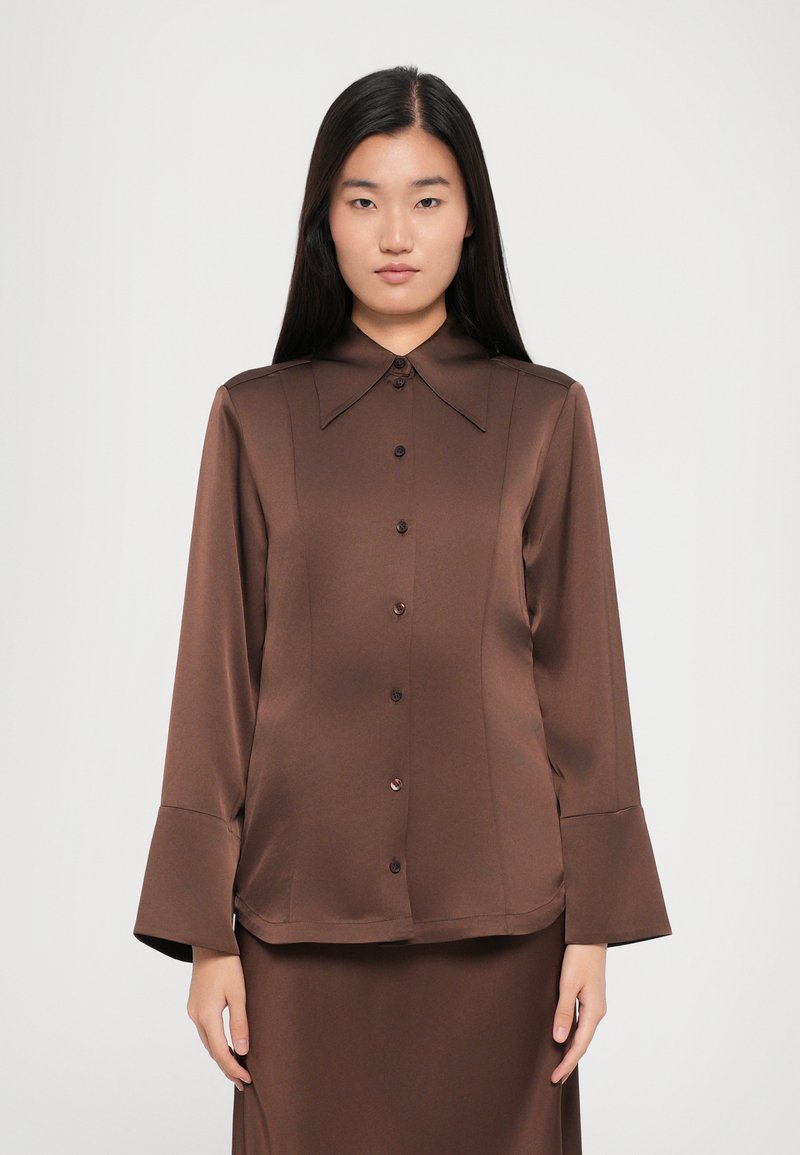 Brown satin blouse featuring a pointed collar, long flared sleeves, and a front button closure with matching fabric-covered buttons.