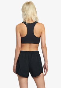 Sort atletisk sportbh med racerback-design, parret med løstsiddende sorte shorts med elastisk talje. Glat stoftekstur.