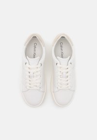 Sneakers bianchi con tomaia in pelle liscia, dettagli in camoscio grigio chiaro sul tallone, lacci piatti e design minimalista. Logo del brand visibile all'interno.