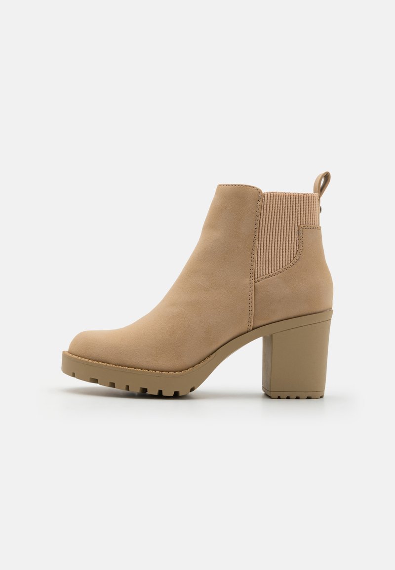 Beige Ankle-Boot aus Wildleder mit einem gerippten elastischen Einsatz, einem Blockabsatz und einer abgerundeten Zehenpartie, ausgestattet mit einer Zuglasche auf der Rückseite.