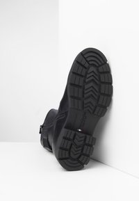 Black leather ankle boot with a textured rubber sole, side zip closure, and logo detail. The sole features a tread pattern for grip.