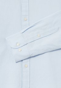 Himmelblaues Hemd aus strukturiertem Baumwollstoff, mit spitzem Kragen, abgerundetem Manschetten mit Knöpfen und dezentem Glanz.