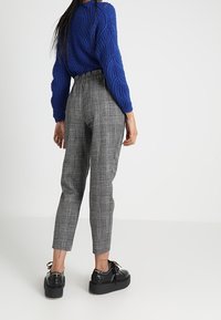 Sinine kaelus-salongi kudum, kõrge vöökoha halli ruudulise lõikega püksid ja mustad platvormkingad. Pükstel on kitsenev istuvus ja nähtavad õmblused.