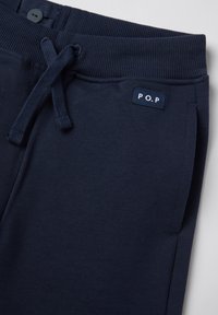 Navyblauwe sportbroek met een ribbelband, verstelbaar trekkoord en zijzakken. Heeft een klein "P.O.P" label op de band.