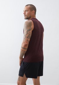 Μαρούλι αμάνικο αθλητικό μπλουζάκι και μαύρη βερμούδα. Το μπλουζάκι έχει υφή, ενώ η βερμούδα διαθέτει πλευρικές σχισμές και ένα μικρό λογότυπο στο στρίφωμα.