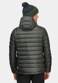 Ciemnozielona kurtka puchowa z poziomymi przeszyciami i dopasowanym kapturem. Noszona z czarną czapką beanie z pomponem.