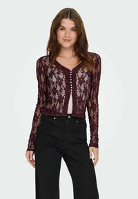 Burgunderfarvet lace cardigan med lange ærmer, der har V-halsudskæring og perleknapper foran; båret over en lys top og parret med sorte bukser.