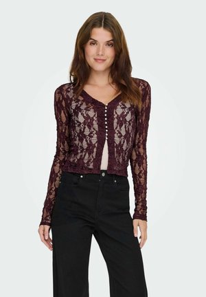 Burgunderfarvet lace cardigan med lange ærmer, der har V-halsudskæring og perleknapper foran; båret over en lys top og parret med sorte bukser.