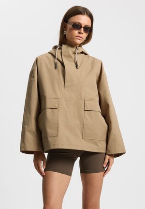 Khaki oversize'owa kurtka z wysokim kołnierzem, dwoma przednimi kieszeniami i kapturem ze ściągaczem. Gładka, lekka tkanina, zapewnia luźne dopasowanie.