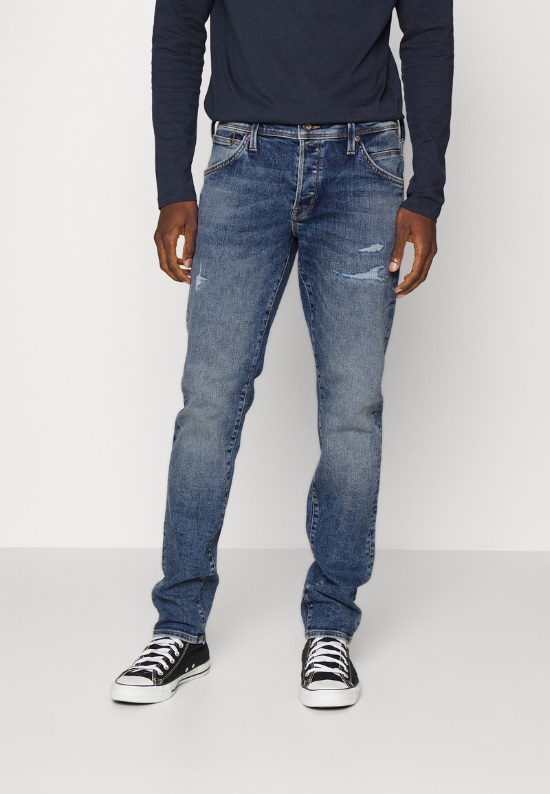 Jeans de denim azul con un corte recto, que presentan detalles desgastados, áreas deslavadas, costuras en contraste y un diseño clásico de cinco bolsillos.