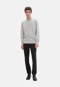 Grijze polo met lange mouwen en kraag, met een twee-knopen sluiting, zachte textuur, gecombineerd met zwarte broek en zwarte schoenen.