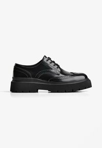 Pantofii din piele neagră, tip brogue, cu talpă groasă cu striații, închidere cu șireturi și cusături decorative perforate, fotografiați pe un fundal alb.
