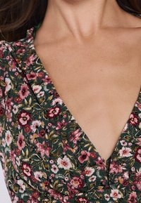 Floral jurk met een diepe V-hals, met een groene achtergrond en roze, witte en rode bloemen. Lichtgewicht stof met een gestructureerd patroon.